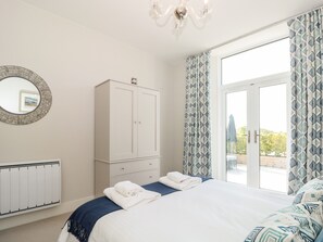 Quarto com cama, guarda-roupa, radiador e uma janela grande com cortinas.
