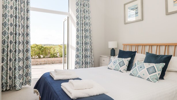 A bedroom with a large bed, patterned curtains, a bedside table with a lamp, and a framed picture on the wall.