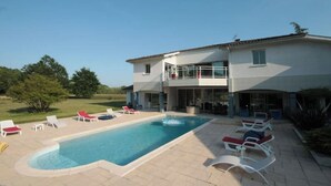 A two-story house with a swimming pool, outdoor seating, and a view of the surrounding landscape.