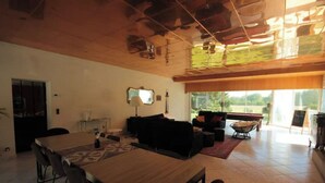 A spacious living area with a wooden dining table, black sofas, and a large window offering a view of the outdoors.