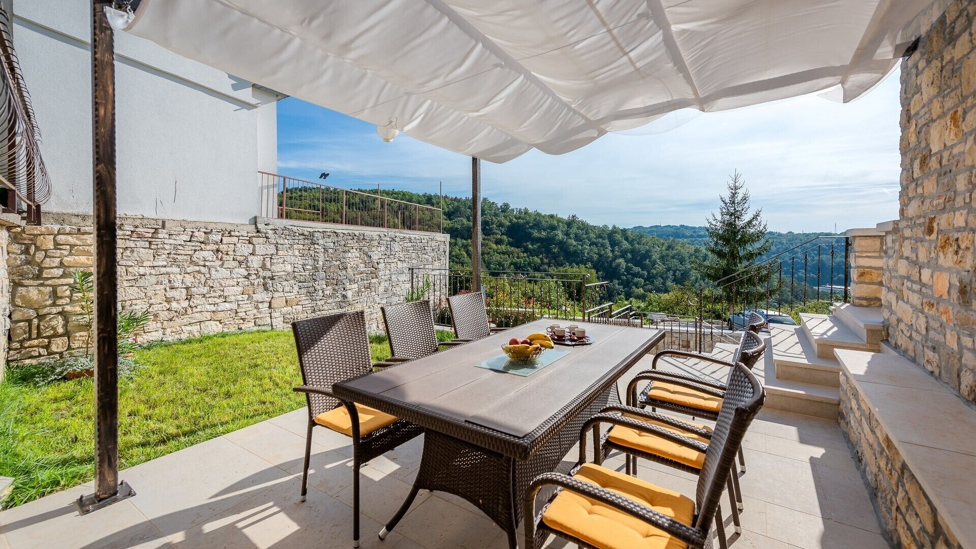 Un patio al aire libre con una mesa y sillas, un toldo blanco y vistas del paisaje circundante.