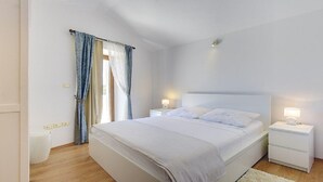 Une chambre avec un grand lit, deux tables de chevet avec des lampes, une fenêtre avec des rideaux et un mur blanc.