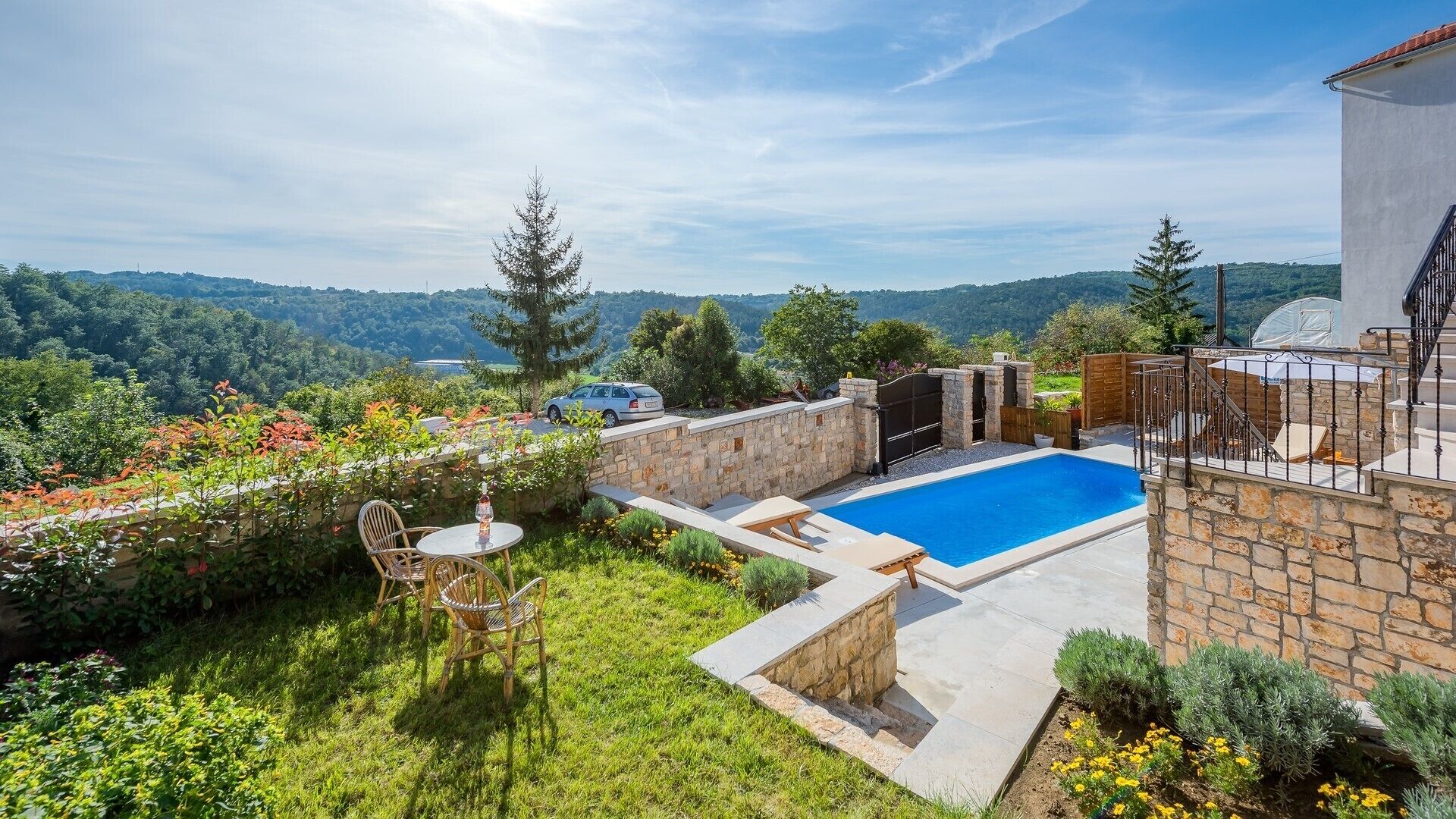 A private pool area with stone walls, a wooden deck, and a view of the surrounding hills.