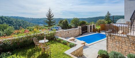 A private pool area with stone walls, a wooden deck, and a view of the surrounding hills.