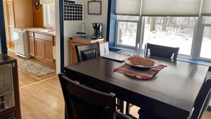 A dining area with a wooden table, chairs, a bowl, and a window with blinds.
