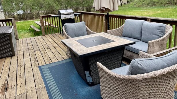 A deck with wicker furniture, a grill, and a view of the surrounding greenery.