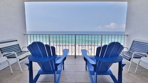 A balcony with two blue Adirondack chairs and a white table, overlooking a beach with a clear sky. - Summit 1218, 1 Bedroom, Beachfront Slps 5 w/Beach Chairs! (Panama City Beach)