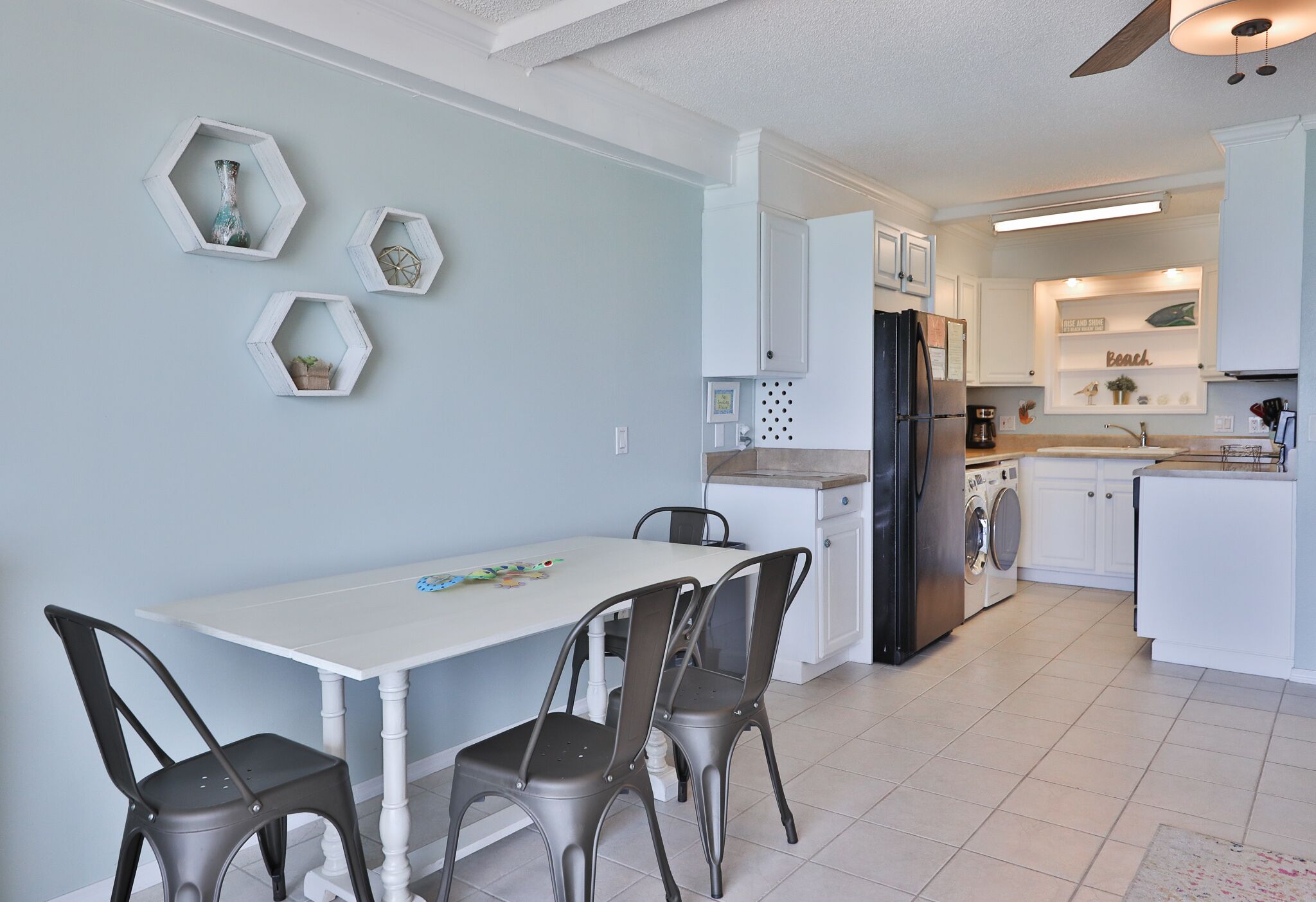 A modern kitchen with white cabinets, a black refrigerator, and a dining area with a white table and four chairs.