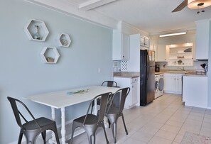 Moderni keittiö, jossa on valkoiset kaapit, musta jääkaappi ja ruokailutila, jossa on valkoinen pöytä ja neljä tuolia.
