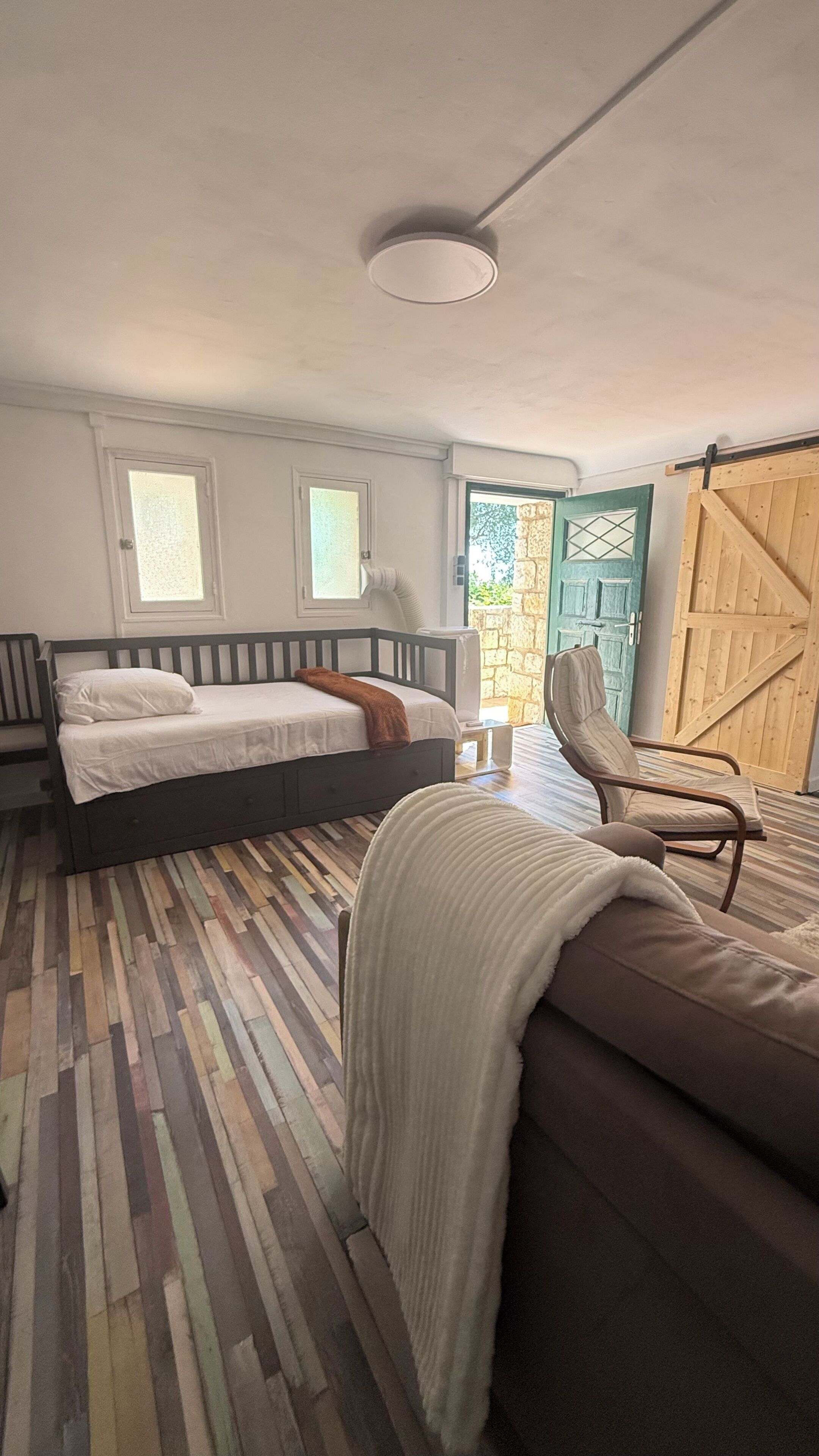 Un dormitorio con cama, una silla, un sofá, suelo de madera y una puerta.