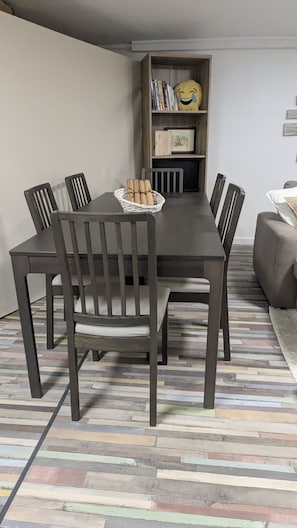 A dining table with six chairs, a basket of bread rolls, and a bookshelf in the background. - Adorable cottage with pool and Ocean view (Nice)