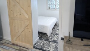 A bedroom with a bed, a TV, a sliding door, and a window. - Adorable cottage with pool and Ocean view (Nice)