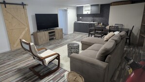 A living room with a sofa, a chair, a television, a kitchen area, and a sliding door. - Adorable cottage with pool and Ocean view (Nice)