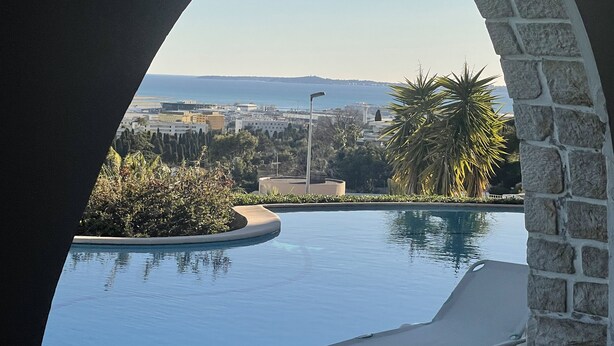A pool with a lounge chair, surrounded by greenery and a stone wall. - Adorable cottage with pool and Ocean view (Nice)