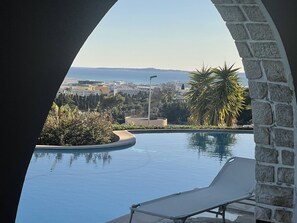 A pool with a lounge chair, surrounded by greenery and a stone wall. - Adorable cottage with pool and Ocean view (Nice)