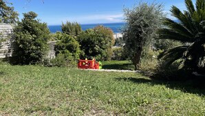 A grassy yard with a red toy truck, trees, and a view of the ocean. - Adorable cottage with pool and Ocean view (Nice)