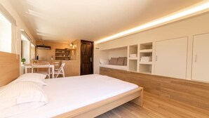 A modern bedroom with a built-in desk, a wardrobe, and a small kitchenette. - Angela's Guest House (AEGINA)