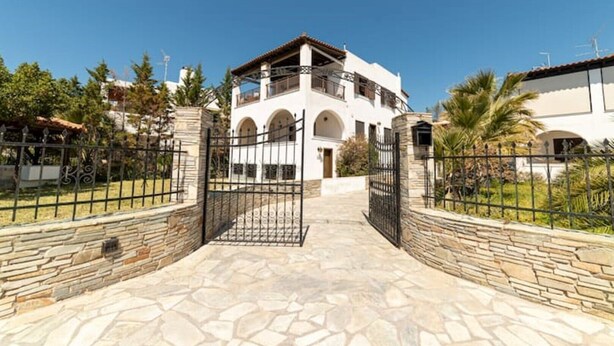 A two-story building with a stone entrance, arched windows, and a balcony. - Angela's Guest House (AEGINA)