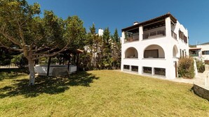 A two-story white building with a covered outdoor seating area and a well-maintained lawn. - Angela's Guest House (AEGINA)