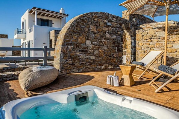 A rooftop pool area with a stone wall, lounge chairs, and a hot tub.