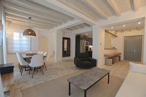 A spacious living area with a dining table, chairs, a sofa, and a bench. There is a kitchen visible in the background.
