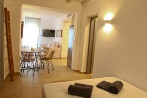 A hotel room with a bed, a dining area with chairs and a table, and a TV in the background.