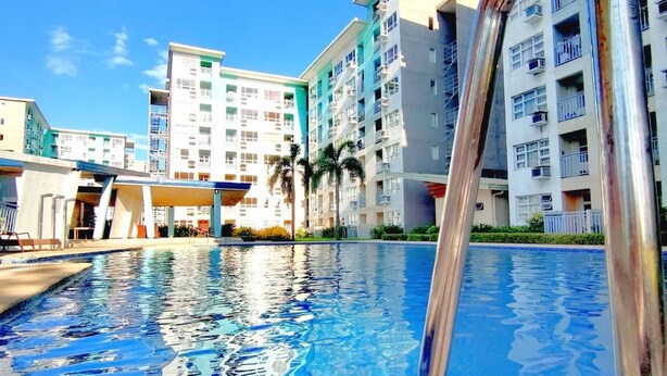 A swimming pool with a metal ladder in the foreground, surrounded by multi-story buildings with balconies and air conditioning units.