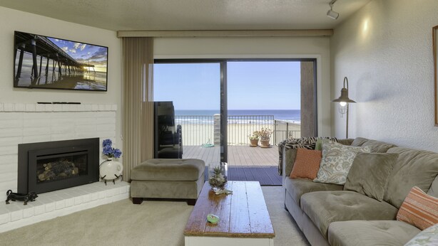 A living room with a fireplace, a sofa, a coffee table, and a large window offering a view of the beach. - Classic California Oceanfront Living (Pismo Beach)