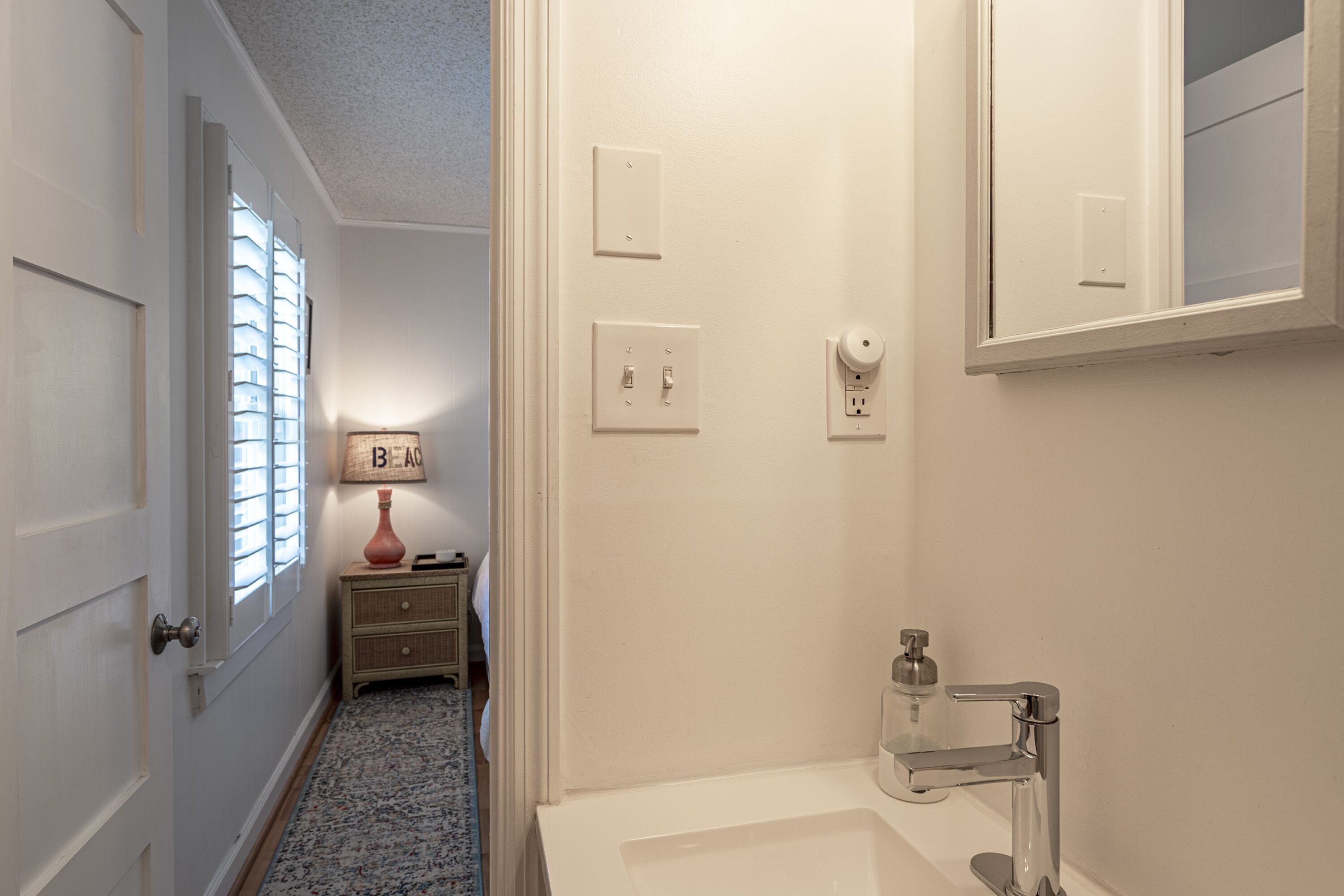 Une salle de bain avec un lavabo blanc, un miroir et une porte donnant sur une autre pièce.