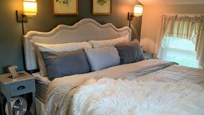 Un dormitorio con una cama grande, dos lámparas fijadas a la pared y dos cuadros enmarcados.