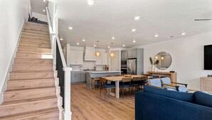 A modern kitchen with a central island, wooden staircase, and a dining area with blue sofas. - Pier 43 At Desert Color: Desert Color Lagoon + Beaches (St. George)