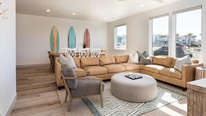 Ein modernes Wohnzimmer mit einem beigefarbenen Ecksofa, einem runden Hocker und einem Essbereich mit einem weißen Tisch und Stühlen.