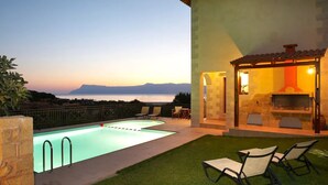 Piscina con vistas al mar y a las montañas, mobiliario exterior y chimenea de piedra.