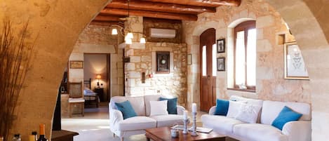 A cozy living room with a stone wall, wooden beams, a white sofa set, and a coffee table.