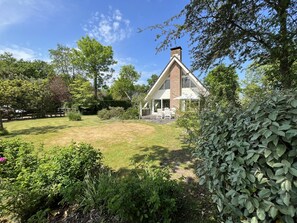 A house with a large lawn, a patio with outdoor furniture, and a brick chimney.