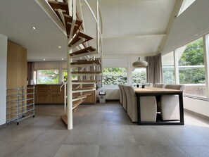Una cocina moderna con una escalera espiral integrada, un comedor con mesa y sillas, y grandes ventanales que ofrecen vistas a zonas verdes.