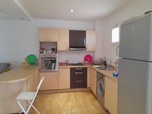 Compact kitchen with oven, microwave, and refrigerator, featuring a sink and dish rack.