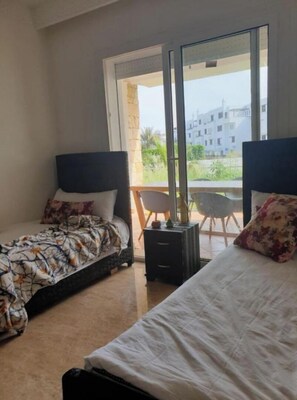 Two single beds with distinct headboards and pillows, a table, and a chair, offer a comfortable retreat with a view of the surrounding area.