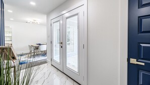 Un pasillo con una puerta azul, paredes blancas y un comedor con mesa y sillas.