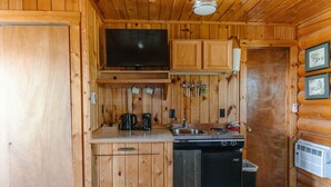 Een compacte keuken met houten wanden, een flatscreen televisie, een spoelbak, een koffiezetapparaat en een vaatwasser.