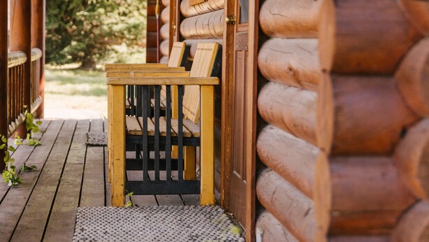 Een houten blokhut met een veranda, een houten bankje en een deur.