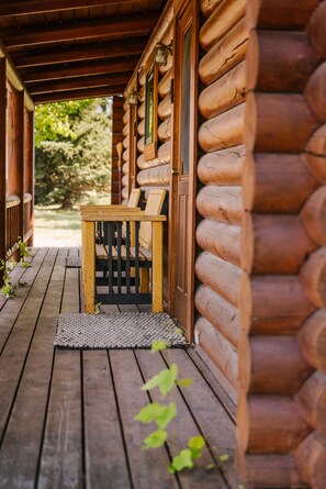 A wooden log cabin with a porch, a wooden bench, and a door. - Bunkhouse 3 at Gallatin Canyon Cabins (Gallatin Gateway)