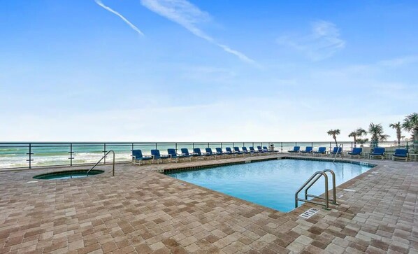 Relax by the oceanfront pool, featuring a rectangular pool and adjacent hot tub, surrounded by lounge chairs.