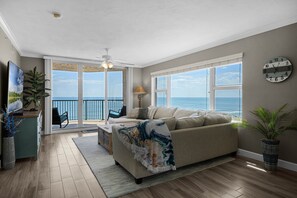 Relax in this inviting living room with a comfortable sofa, ceiling fan, and ocean views from the balcony.