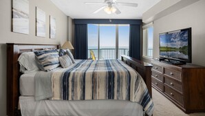 Een slaapkamer met een groot bed, een plafondventilator, een televisie en uitzicht op de oceaan.