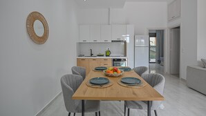 A modern kitchen with white cabinets, a wooden dining table with four chairs, and a fruit bowl on the table. - Moka Apartments (Chania)