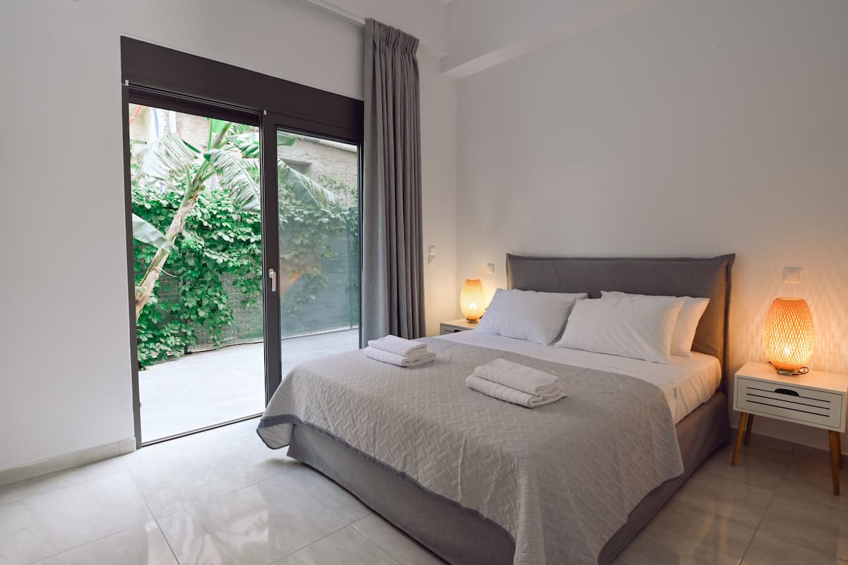 A modern bedroom with a large bed, a sliding glass door to a balcony, and a bedside table with a lamp.