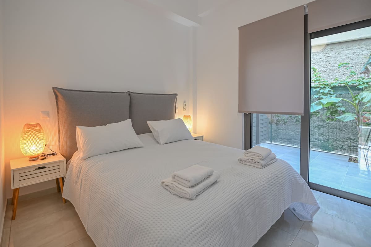 A modern bedroom with a large bed, white bedding, and a nightstand with a lamp.