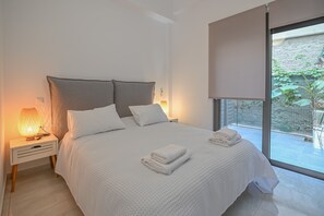 Un dormitorio moderno con una cama grande, ropa de cama blanca y una mesita de noche con lámpara.