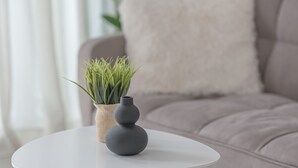 A modern living room with a white round table, a grey vase, and a green plant on a light grey sofa with a fluffy pillow. - Moka Apartments (Chania)